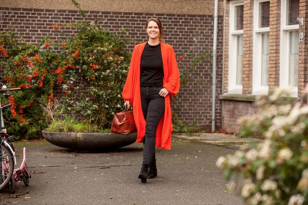 Vrouw met rood lang vest lopend voor pand