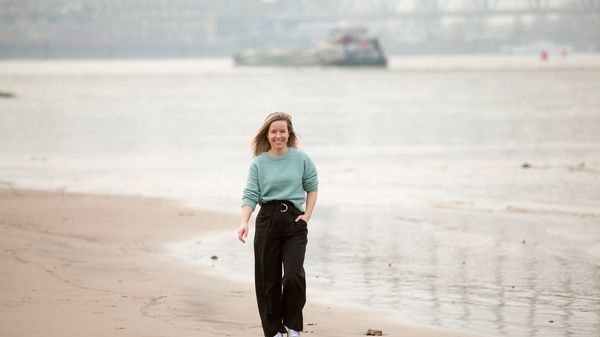 Vrouw lopend over het strand met schip op achtergrond