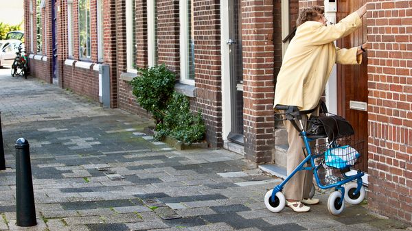 vrouw met rollator doet van buiten af haar voordeur open met sleutel