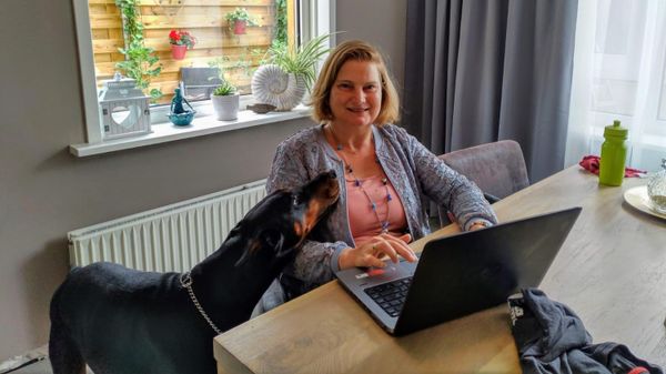 vrouw achter tafel met laptop en hond naast zich