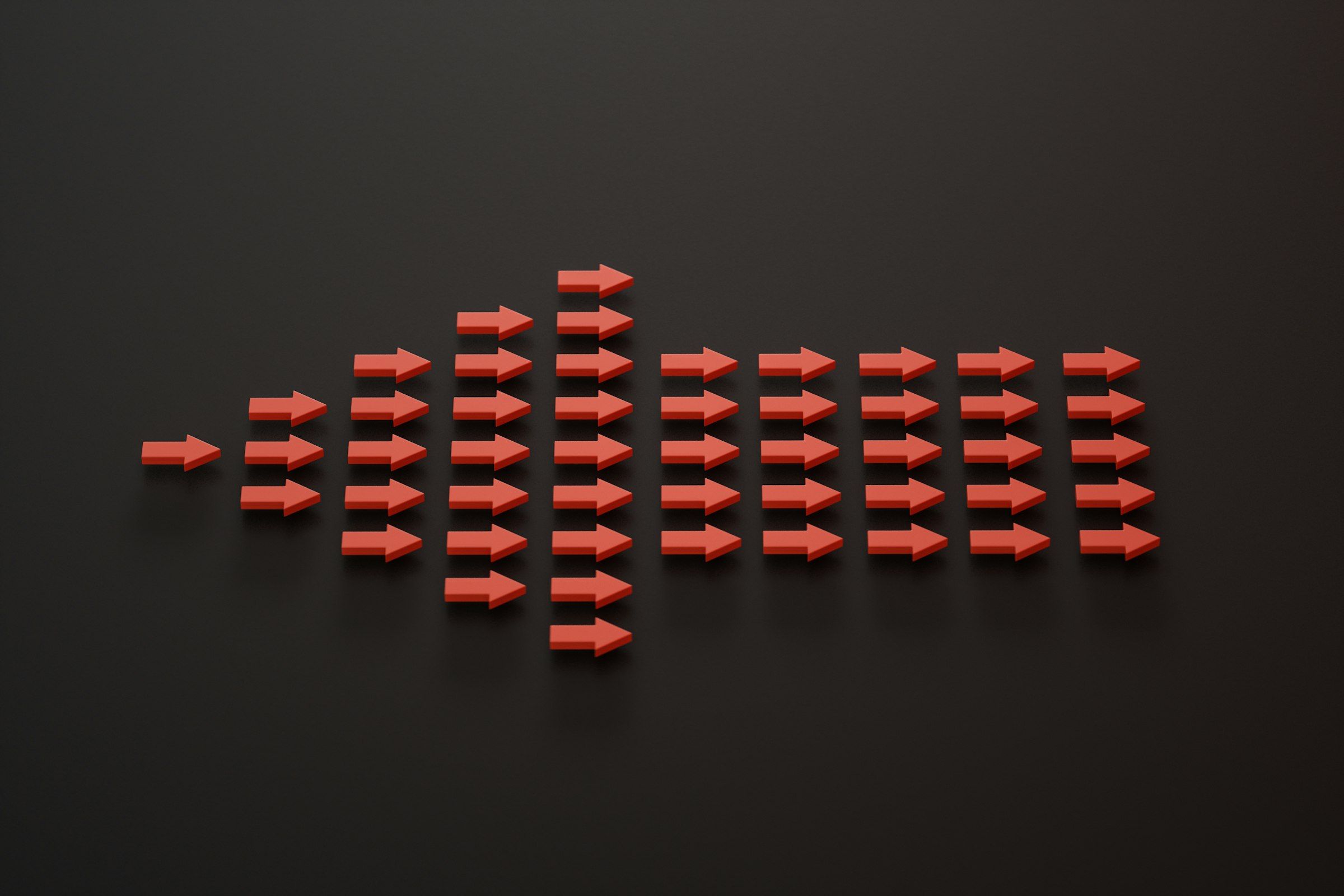 A single small arrow growing into a larger formation of red arrows on a dark background