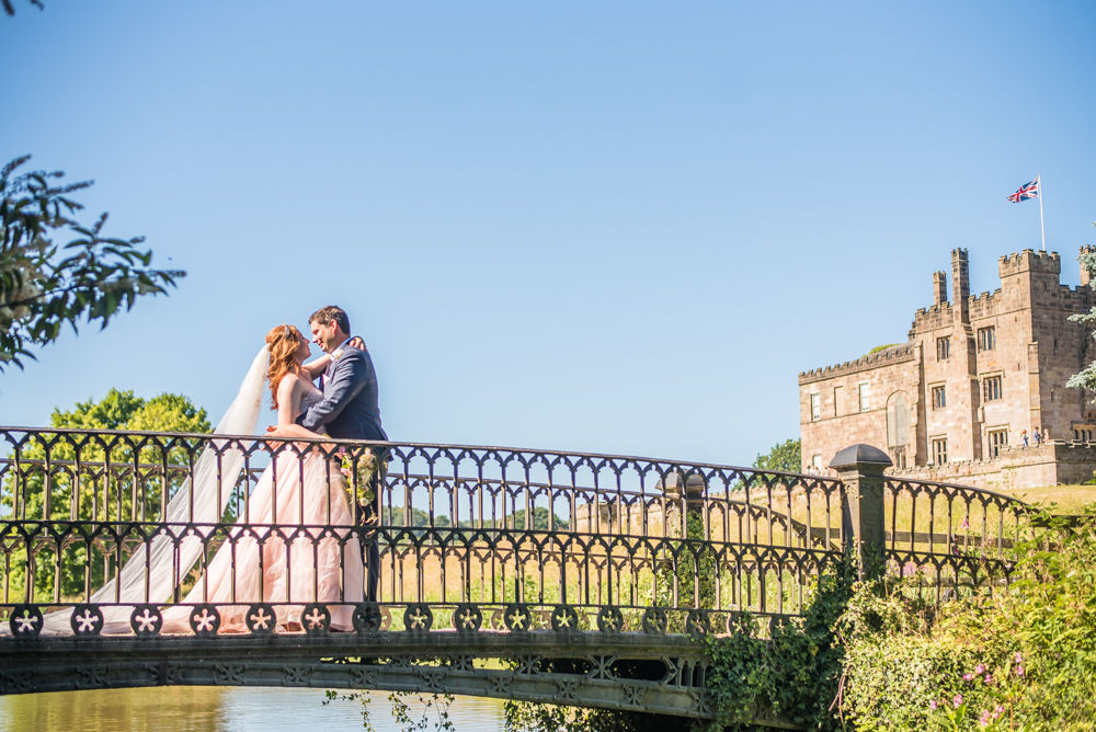 Bride and groom kissing on bridge with castle in background, Ripley Castle weddings, Yorkshire wedding photographers