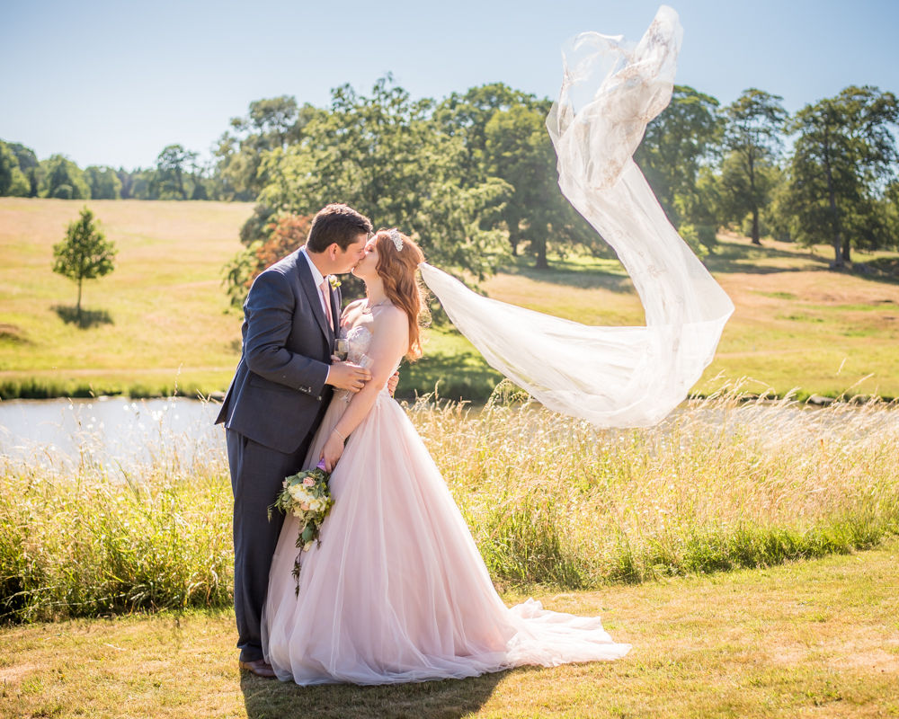 Bride's veil blowing while they kiss in castle grounds, Ripley Castle weddings, Yorkshire wedding photographers