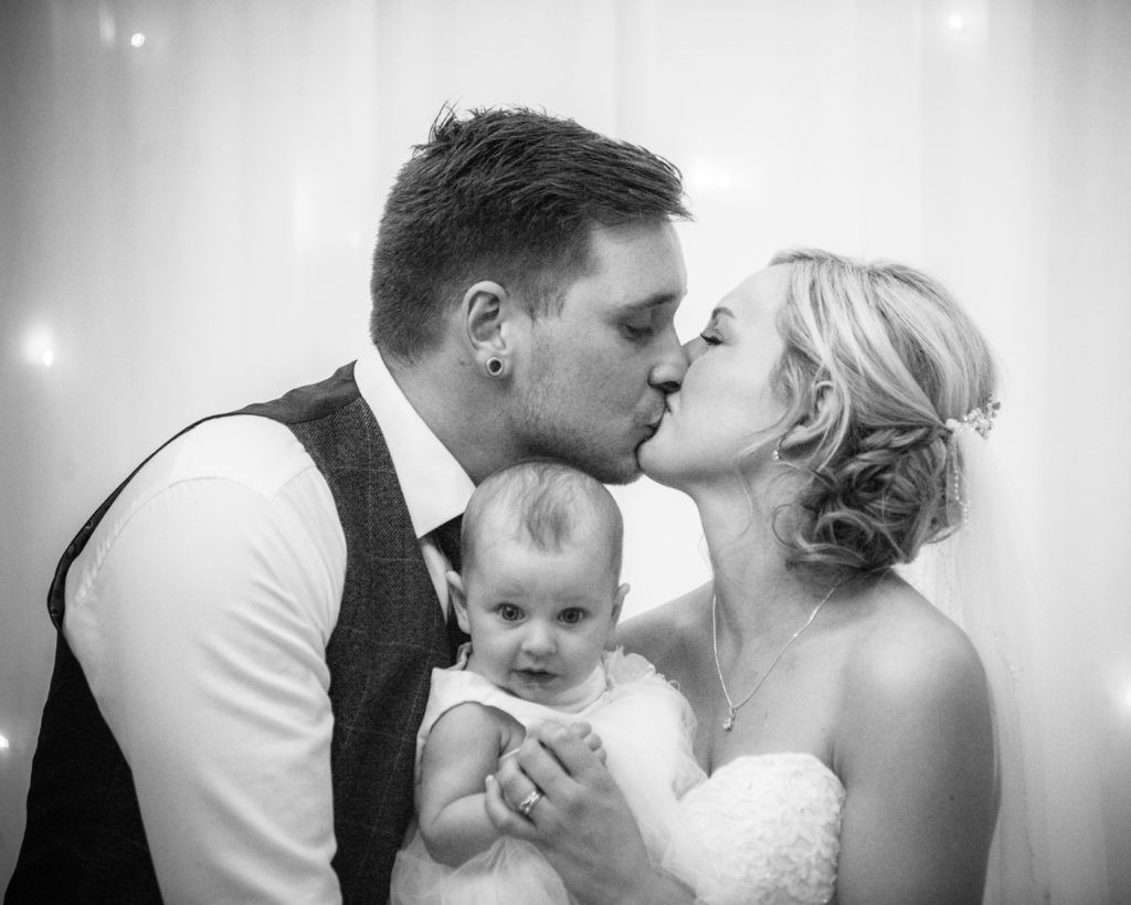 Bride and groom kiss with daughter in the middle, Wortley Hall, Sheffield wedding photography