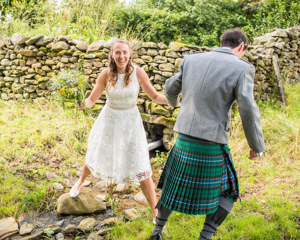 Bride jumping over stream, Sedbergh weddings, Lake District photography