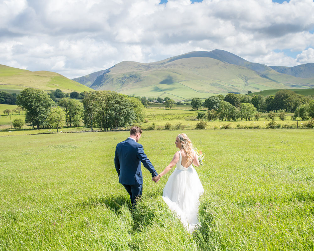 Camilla and Damian walking through fields, Lake District wedding photographers