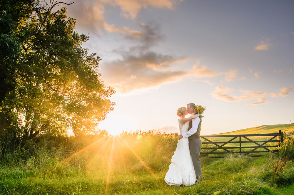 Verity and Adam kissing in field with sunset, Smallshaw Farm Cottages weddings, Sheffield wedding photography