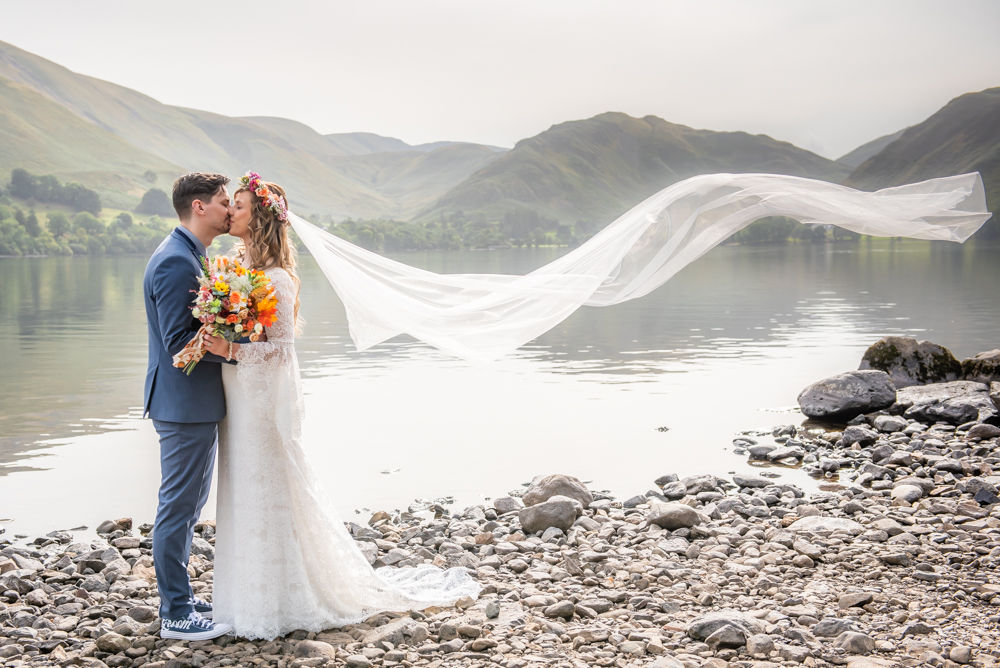 Bride's veil blowing as couple kiss by Lake, Ullswater elopement wedding, Macdonald Leeming House