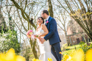 Groom cuddling bride who is laughing in front of daffodils, Penrith wedding, Lake District