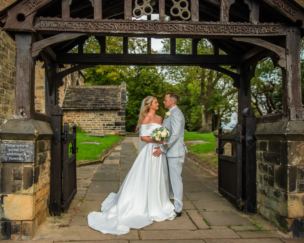 Bride and groom cuddle under church arch, Tankersley Manor weddings Sheffield