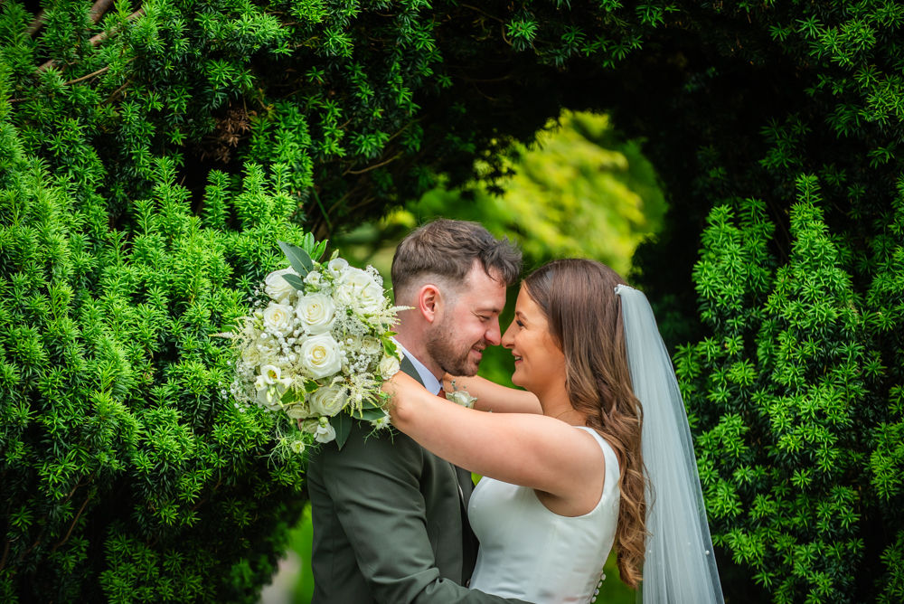 Bride and groom snuggle heads under bush, Castle Green Hotel weddings, Cumbria photographers
