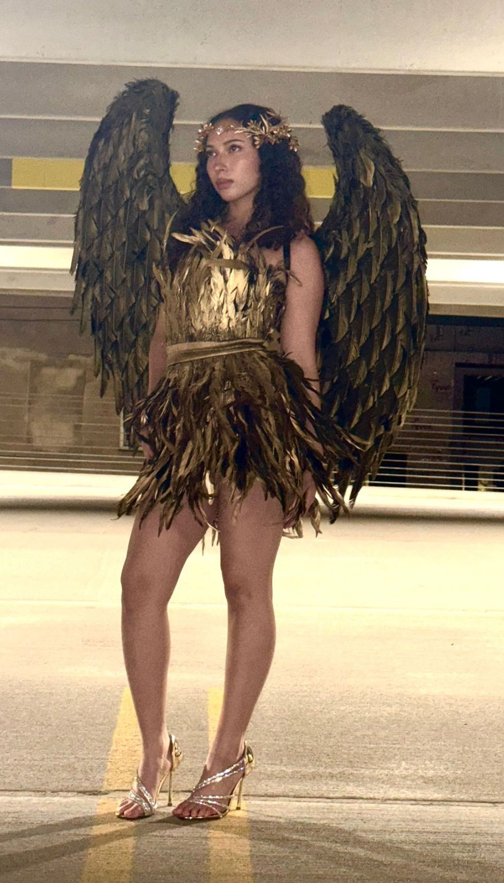 Modeled golden angel costume with sculptural black wings, a feathered mini dress, and a floral crown.