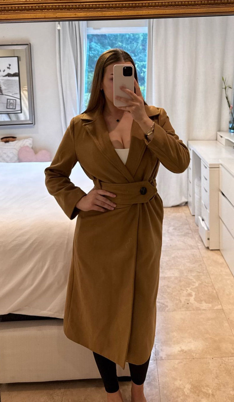 Camel belted wool coat worn over a light top and black leggings.