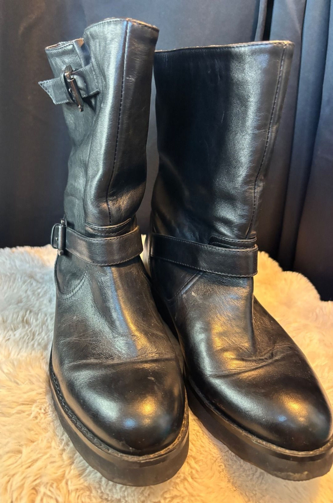 Black leather moto boots with sturdy lug soles, wide ankle straps, and multiple metal buckles.