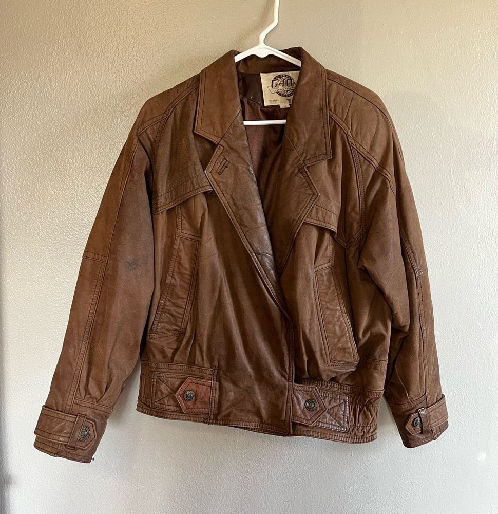 Vintage brown leather bomber jacket with a pointed collar, textured panels, and flap pockets.