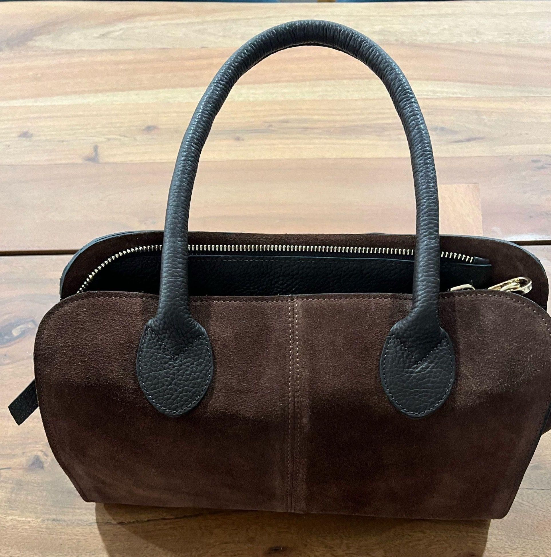 Chocolate-brown suede shoulder bag with a long, low silhouette and black handles.