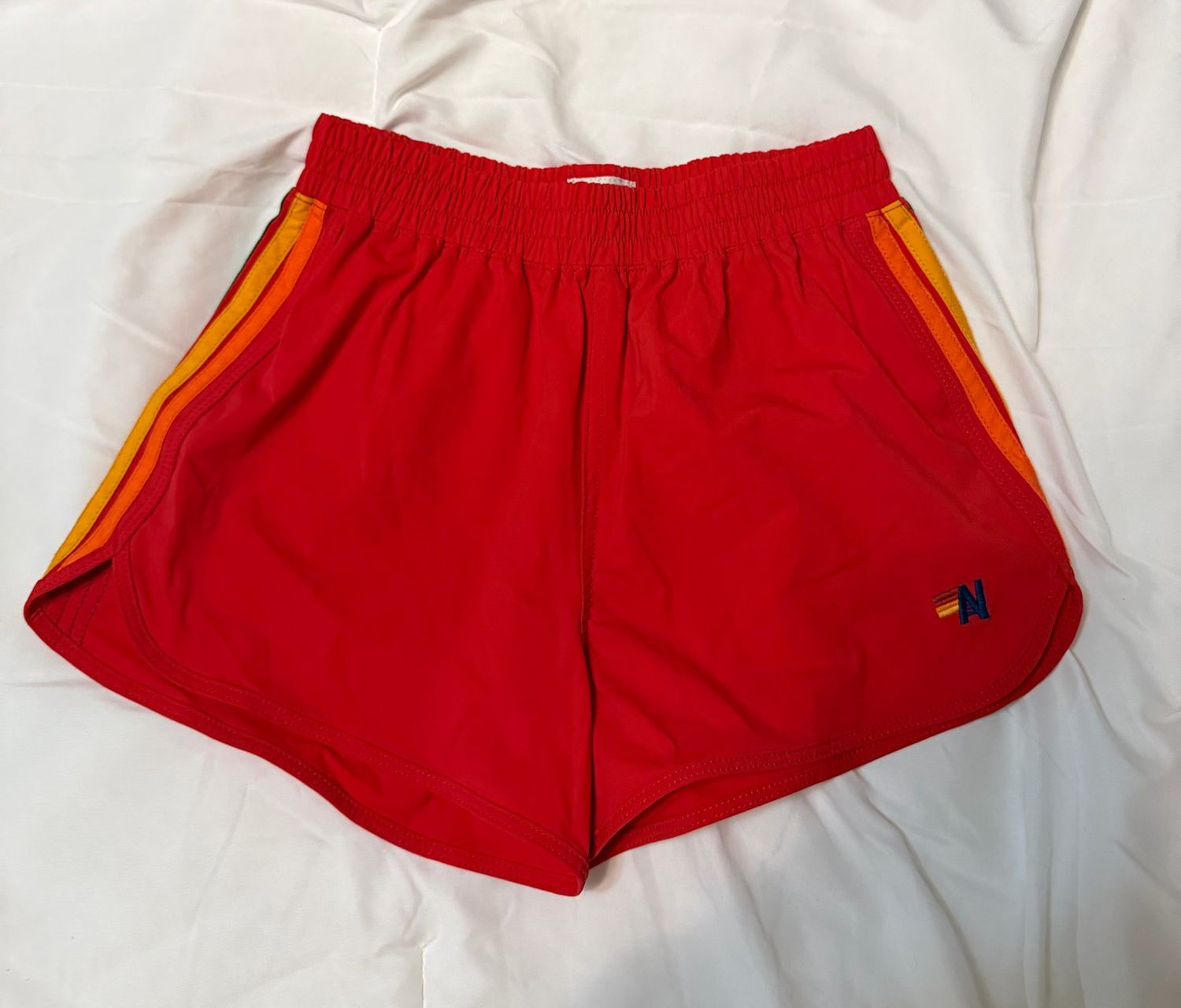 Bright red retro athletic shorts with yellow side stripes and contrast trim.