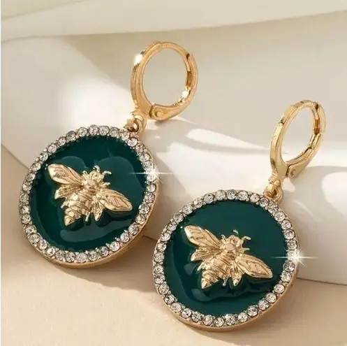 Earrings featuring a raised gold bee design on a glossy dark green background