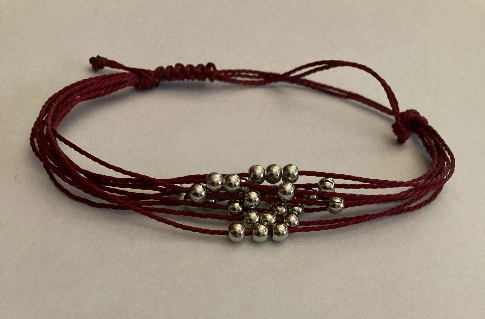 silver beads are threaded along row after row of shiny red cording around the wrist - Image 3