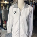 Arena windbreaker full zip jacket raincoat long sleeve tie cuff white grey NWT  New with tag  Same day shipping  Smoke and pets free  This  windbreaker jacket is perfect for outdoor enthusiasts who want to stay comfortable and stylish in any weather. The adjustable tie hem and full zip closure and water-resistant feature make it a great choice for rain or shine. The jacket has a short length with a tie cuff, and the white and grey color combination with the logo accents give it a trendy look.   The jacket is made of 100% polyester and is available in men size XS/ woman size M. It is suitable for both men and women, making it a versatile piece for any wardrobe. Whether you're running errands or hitting the trails, this  windbreaker is the perfect choice. Photo 6