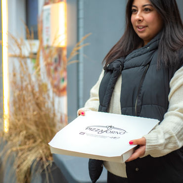 A girl holding a PizzaForno pizza box outside