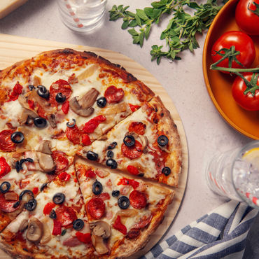 An overtop view of a PizzaForno pizza with tomatoes and a lemonade beside it