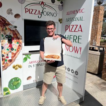 A man standing in front of a PizzaForno machine showing off his pizza.