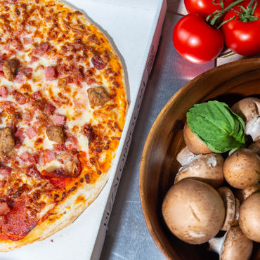 An overtop view of a Meat Lovers pizza with mushrooms and tomatoes beside it