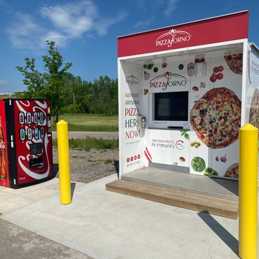 An outdoor PizzaForno kiosk with a vending machine beside it.