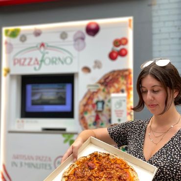 A women holds up a box with a pizza in it.