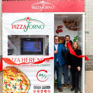 The mayor cutting a ribbon in front of an outdoor kiosk.