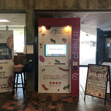 An indoor pizza vending machine with promotional signs beside it
