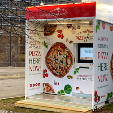 An outdoor pizza vending machine with the sun setting behind it.