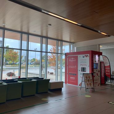 An indoor pizza vending machine in a room that has lots of windows.