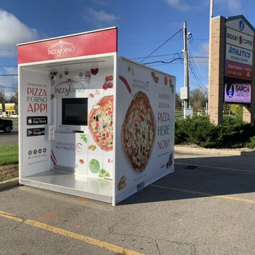 A pizza vending machine that is located on the side of a parking lot