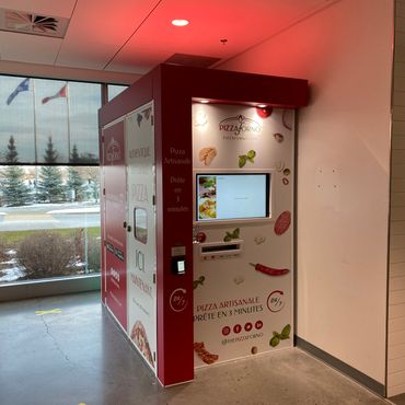 An indoor pizza vending machine that is up against a wall.