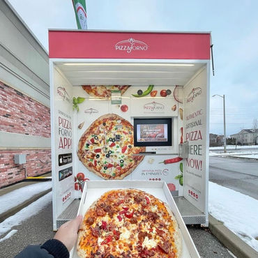 A picture of a man holding a pizza in front of an outdoor pizza vending machine
