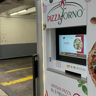 A PizzaForno ATM style kiosk located beside a parking garage
