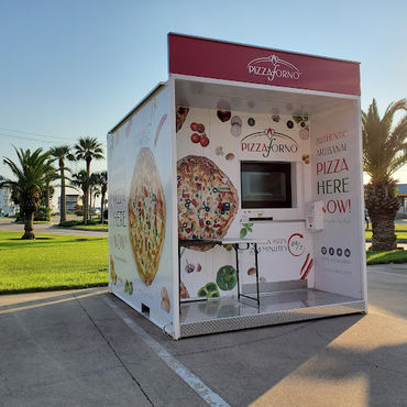 A pizza vending machine that is outside in a warm climate with palm trees behind it.
