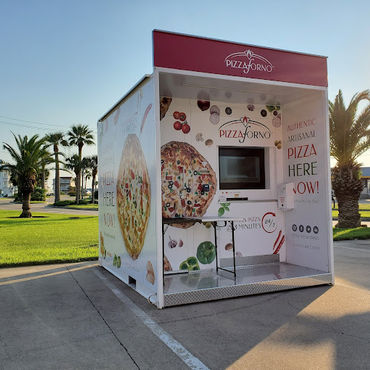 A pizza vending machine that is outside in a warm climate with palm trees behind it.