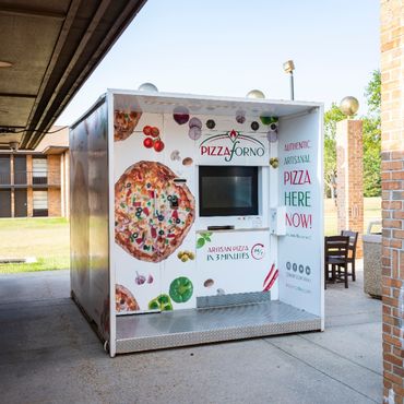 An outdoor pizza vending machine located beside a building