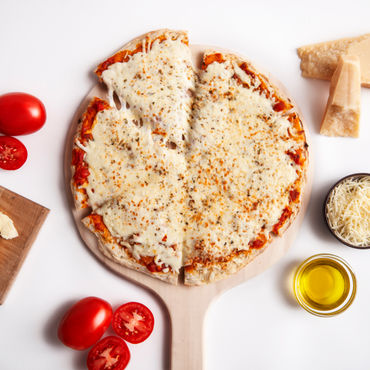 An overtop picture of a cheese pizza on a round wooden cutting board with the toppings in bowls beside it