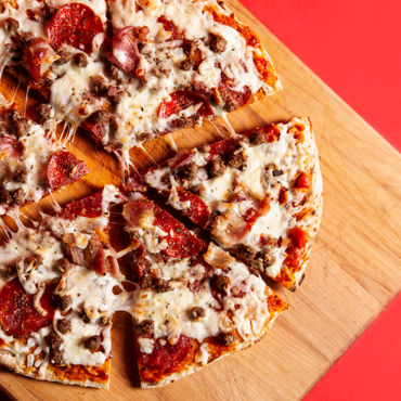 A picture of a Meat Lovers pizza on a wooden cutting board, cut into 6 large slices.