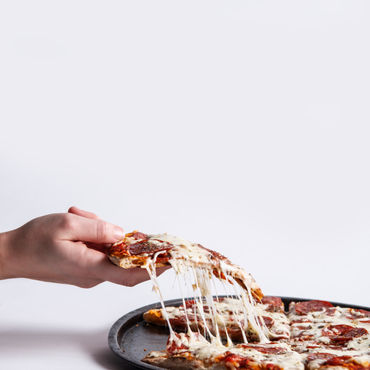 A person taking a slice of a Pepperoni pizza with the cheese melting off.