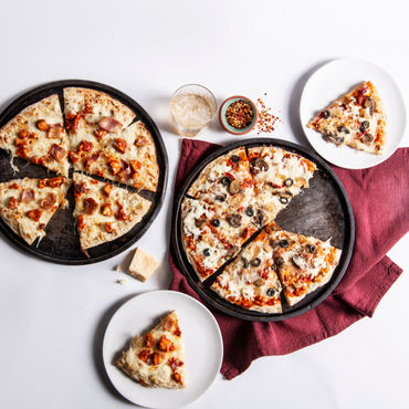 A picture of two pizzas on a white table with slices cut out of each of them.