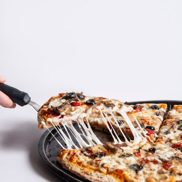 A person taking a piece of pizza from a black cutting board.