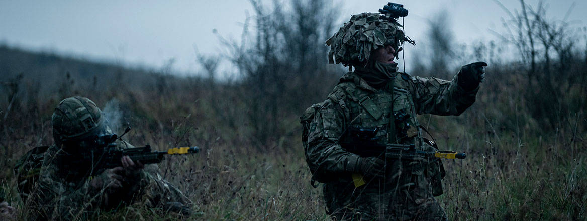 Two soldiers, one pointing a weapon, on a training field