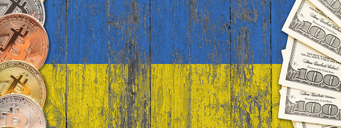 Bitcoins and dollar notes on a worn wooden panel painted with Ukrainian flag
