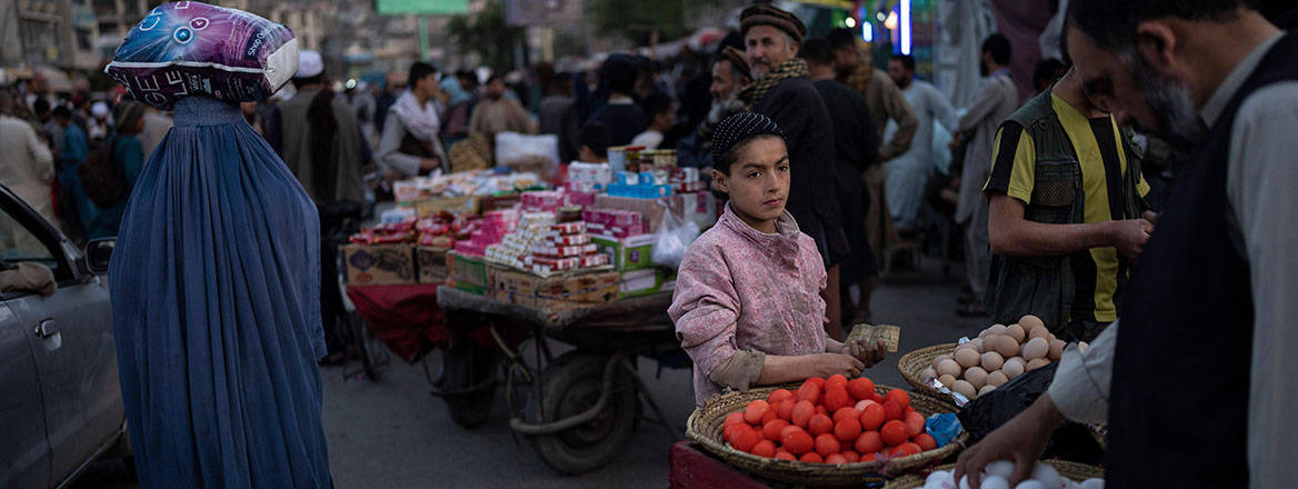 Boy standing at dyed eggs market stall in downtown Kabul women and men passing by