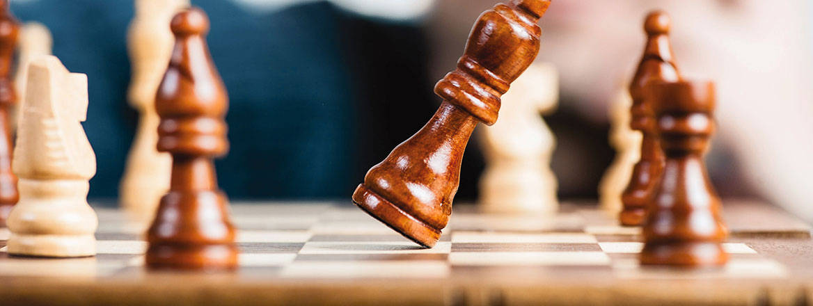 Chess pieces on a board with one tilting and about to fall over.